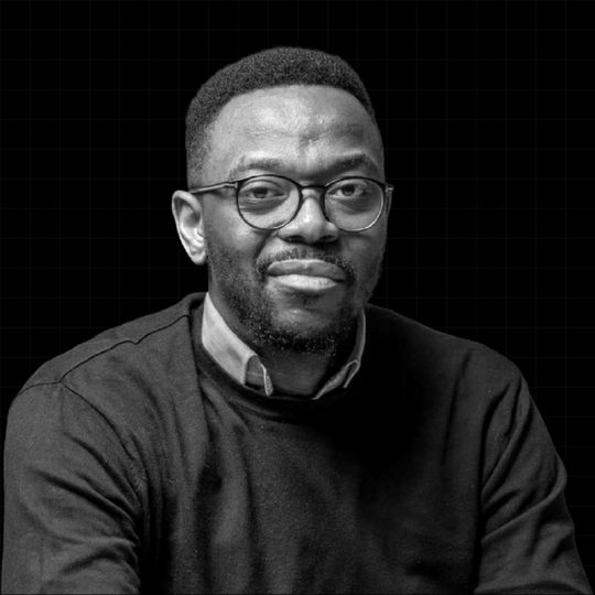Portrait en noir et blanc de Rémy Muzembo, lunettes et pull sombre.